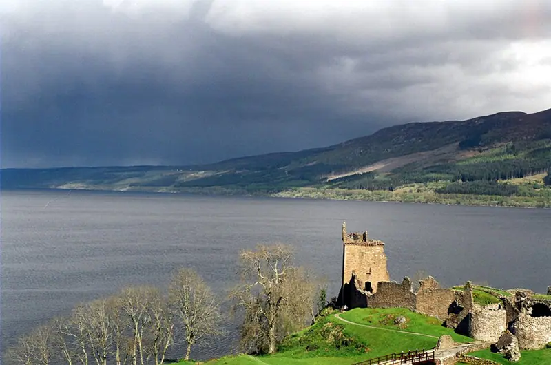 Castle ruins on the shore of a dark loch under stormy skies