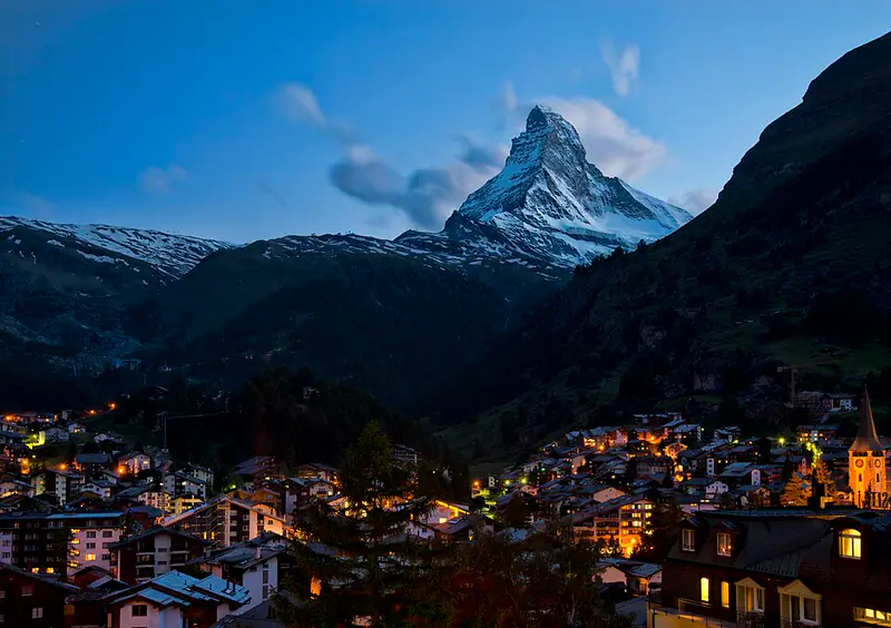 Lit-up mountain village below a pyramid-shaped snowy peak