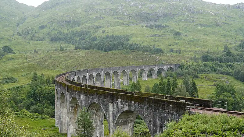 Curved stone railway viaduct across a green glen